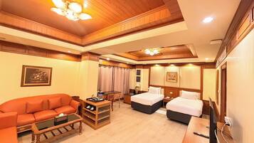 A hotel room with a sofa, two beds, a desk, and a television.