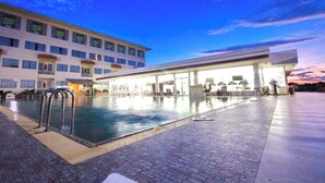 Ein Hotelpoolbereich mit großem Pool, Liegestühlen und einem mehrstöckigen Gebäude mit Fenstern.