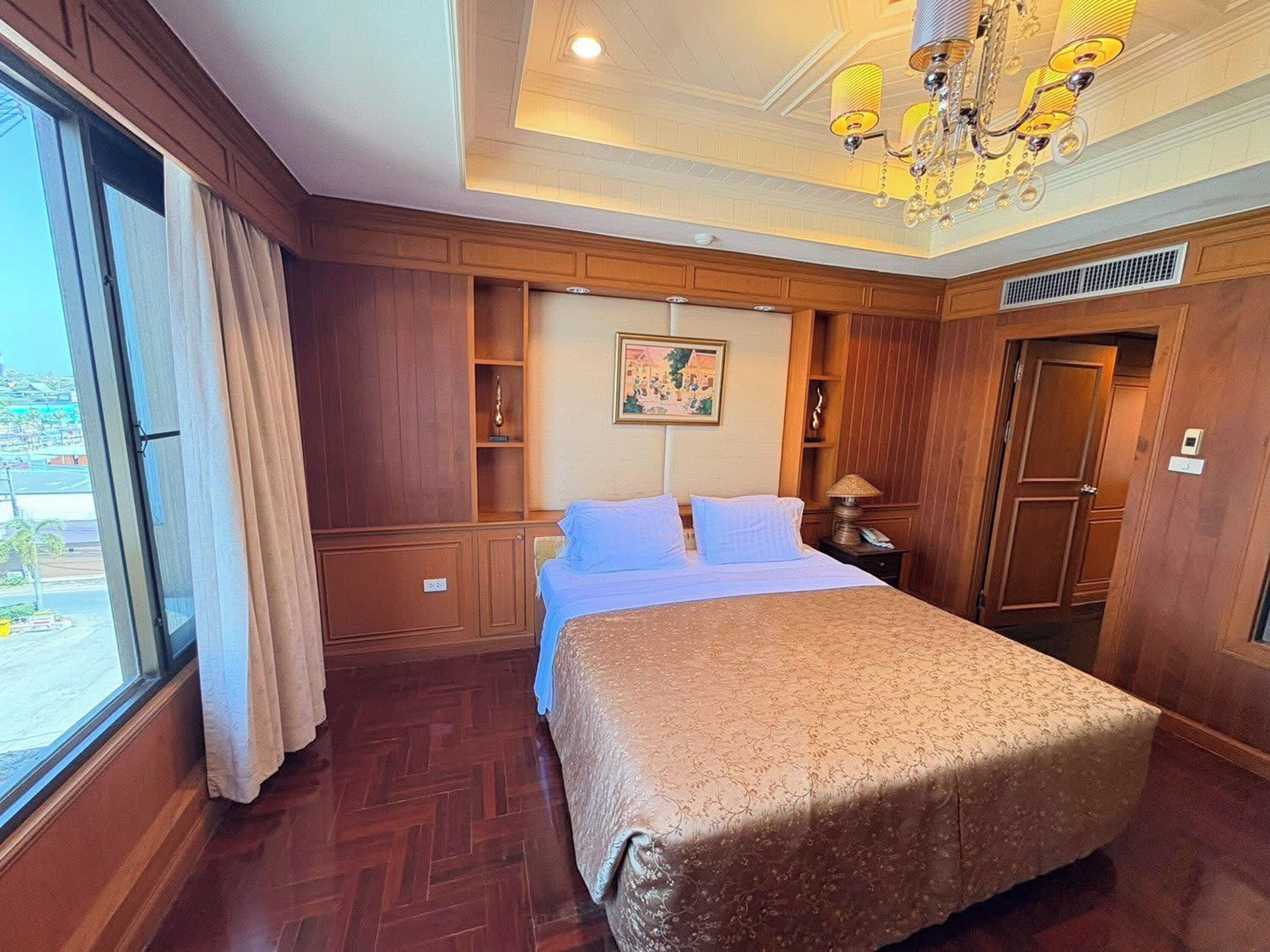 Habitación de hotel con una cama grande, paneles de madera, una araña y un cuadro en la pared.