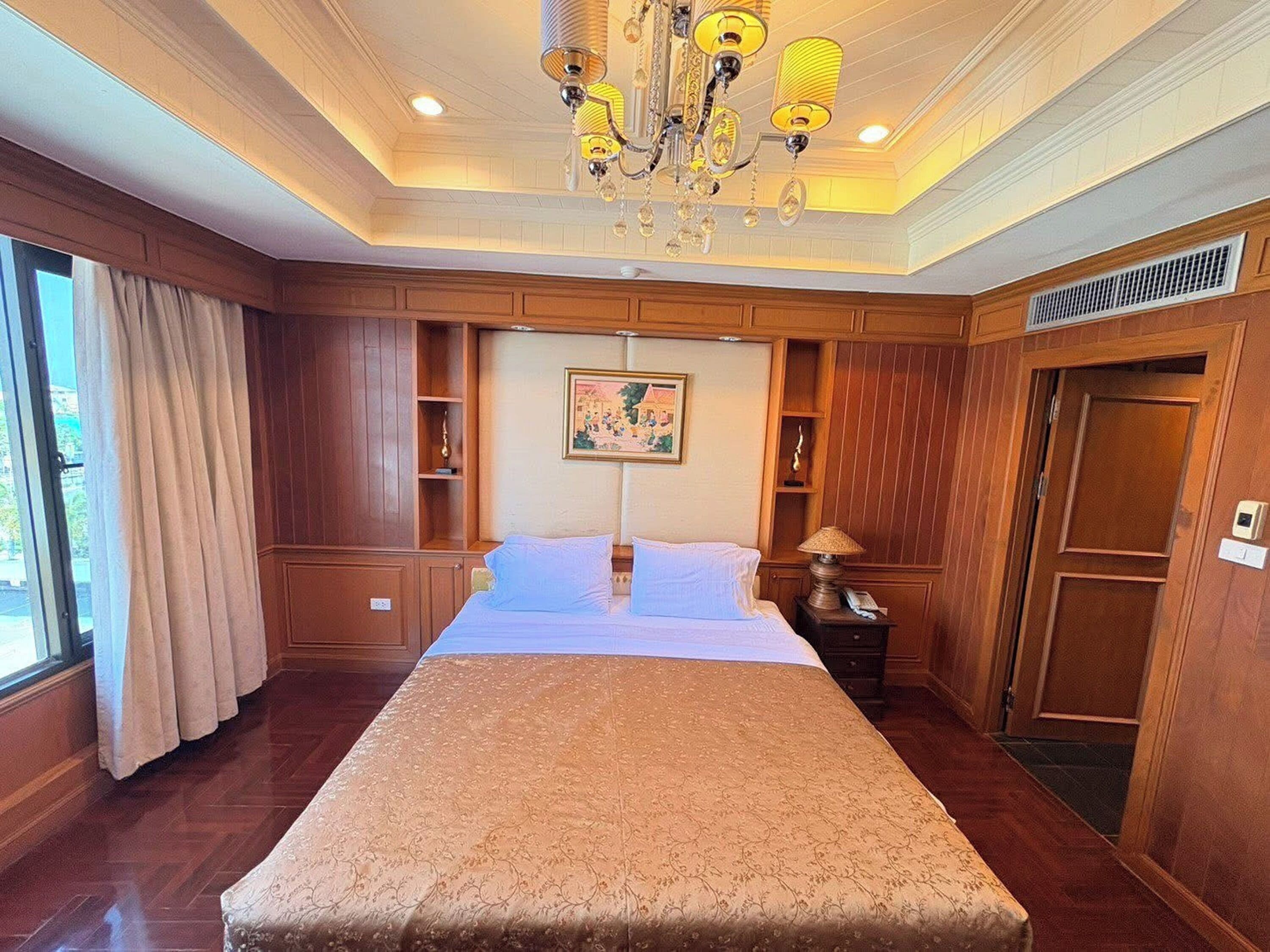 Una habitación de hotel con una cama grande, paneles de madera, un candelabro y un cuadro en la pared.