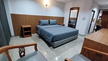 A hotel room with a bed, two bedside tables, a mirror, a wooden desk, and two chairs.