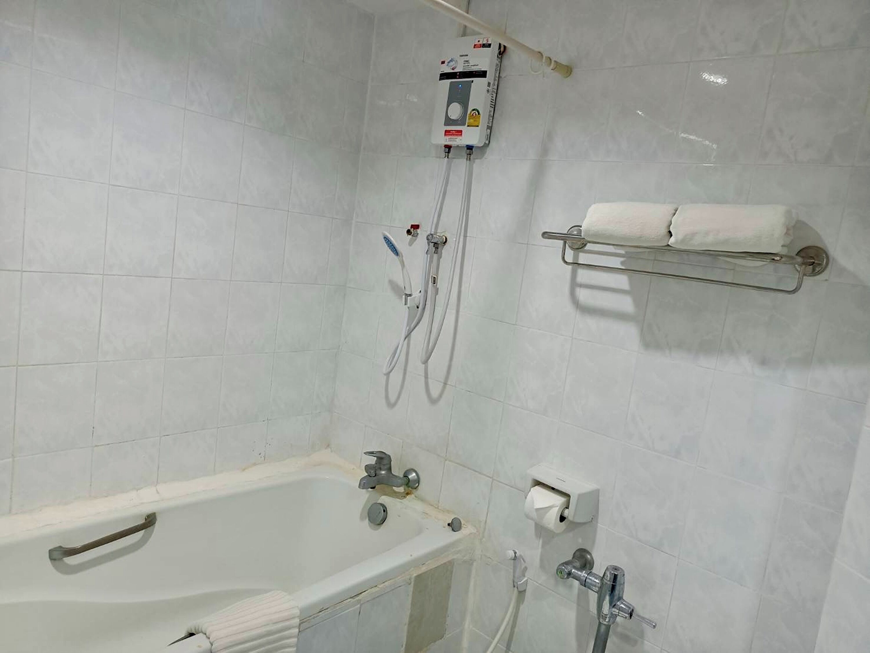 Et badeværelse med badekar, bruser og toilet. Der er en håndklædestang med et håndklæde.