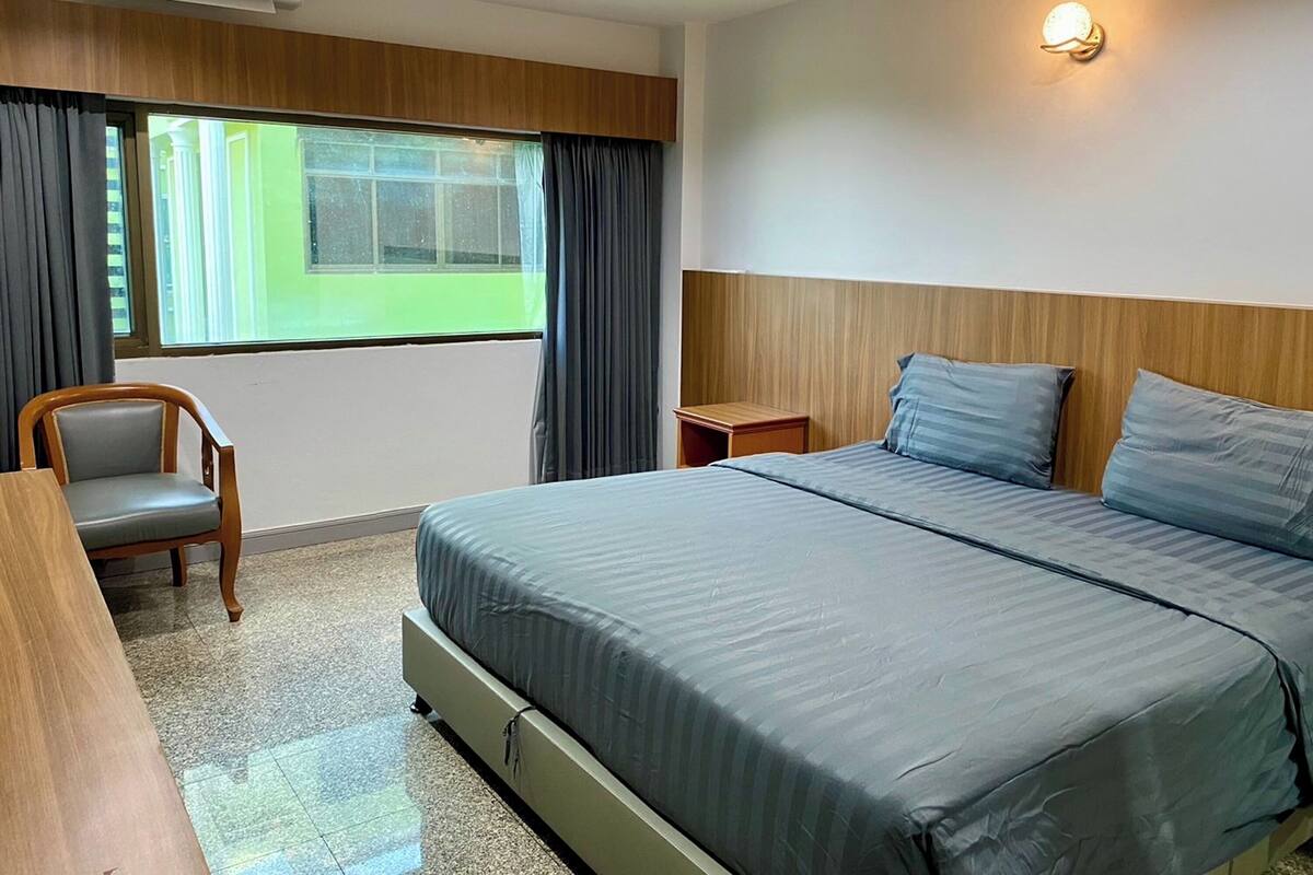 Ein Hotelzimmer mit einem großen Bett, einem Sessel, einem Nachttisch und einem Fenster mit Vorhängen.