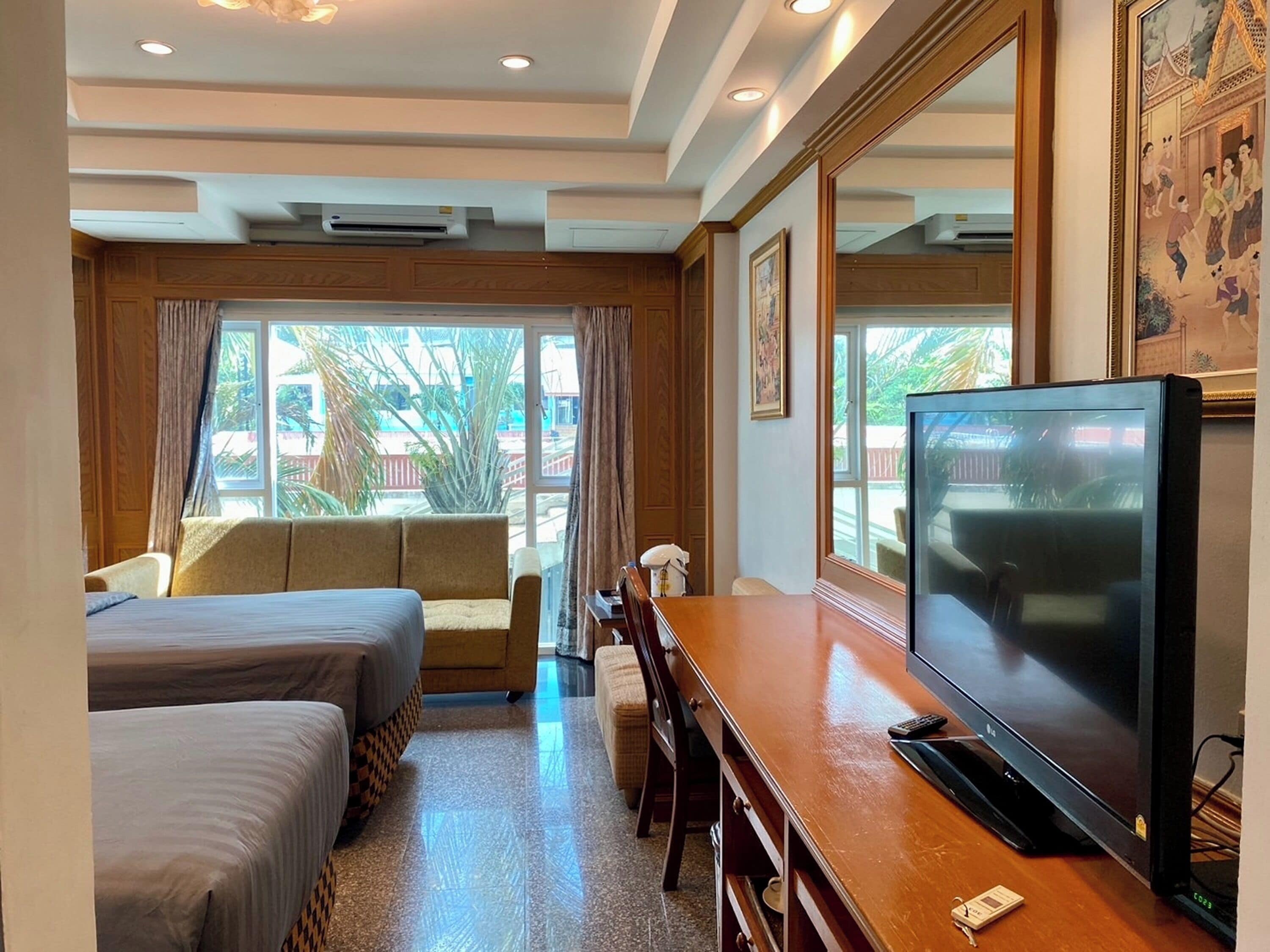 A hotel room with two beds, a sofa, a TV, and a large window with a view of palm trees.