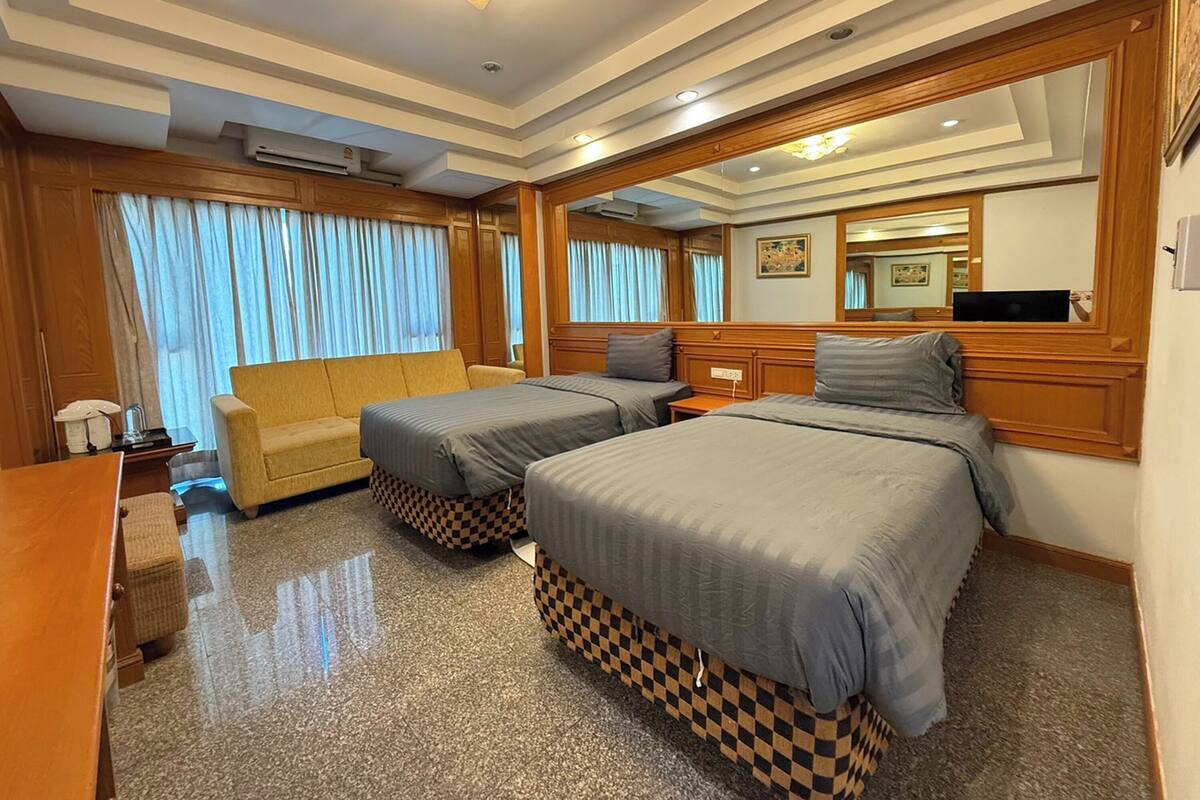 Ein Hotelzimmer mit zwei Betten, einem Schlafsofa, einem Schreibtisch und einem großen Spiegel.