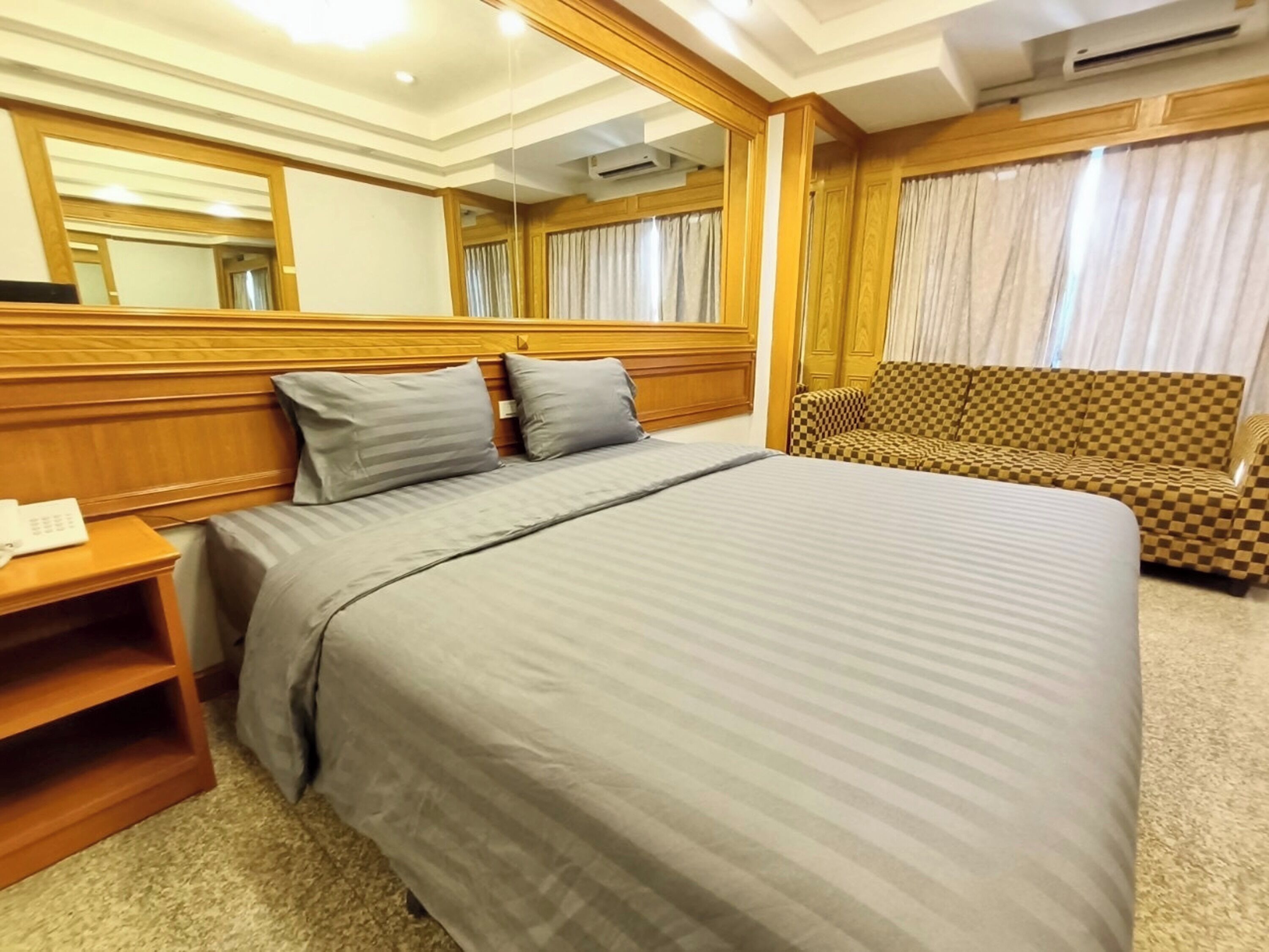 Una camera d'albergo con un letto grande, una testiera di legno, un divano a scacchi e uno specchio.