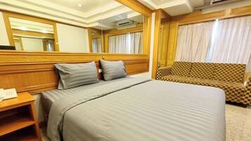 A hotel room with a large bed, a wooden headboard, a checkered sofa, and a mirror.