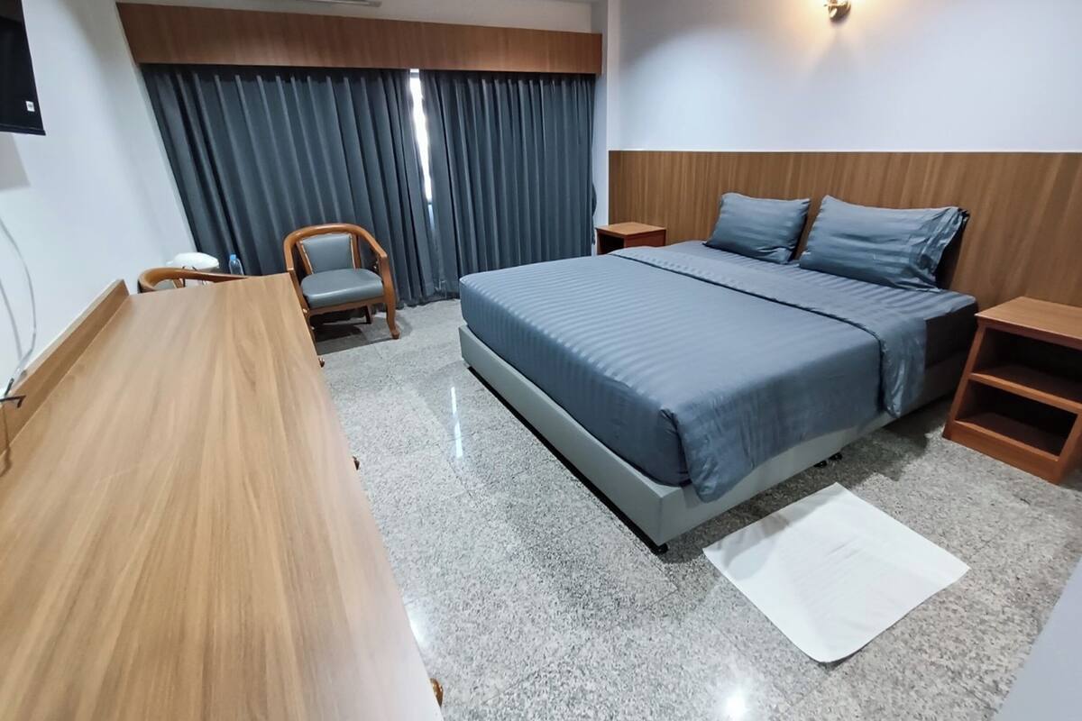 Ein Hotelzimmer mit Bett, Schreibtisch, Stuhl, Nachttisch und Wandklimaanlage.