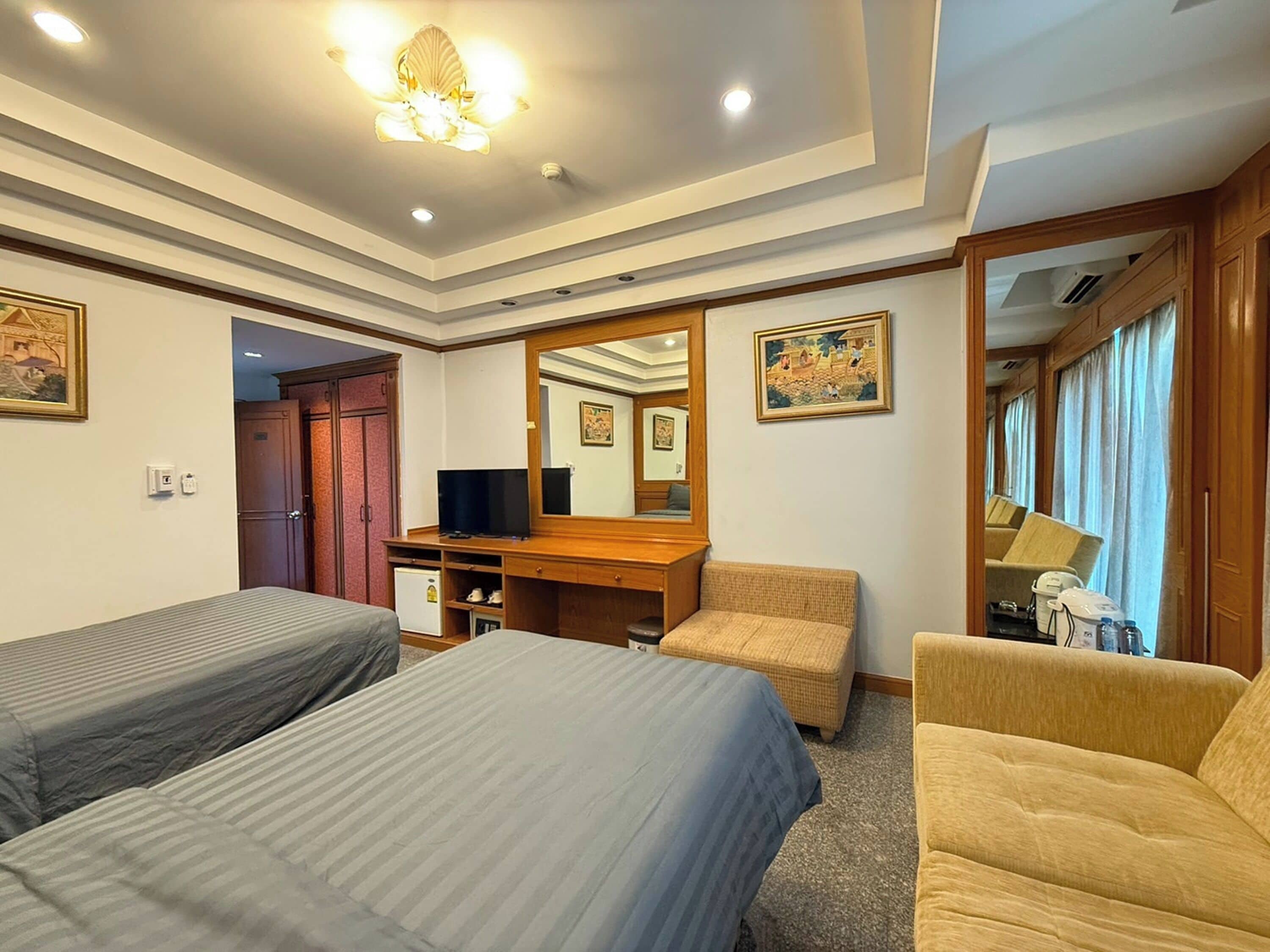 A hotel room with two single beds, a wooden desk with a television, a mirror, and a window with curtains.