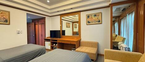 A hotel room with two single beds, a wooden desk with a television, a mirror, and a window with curtains.