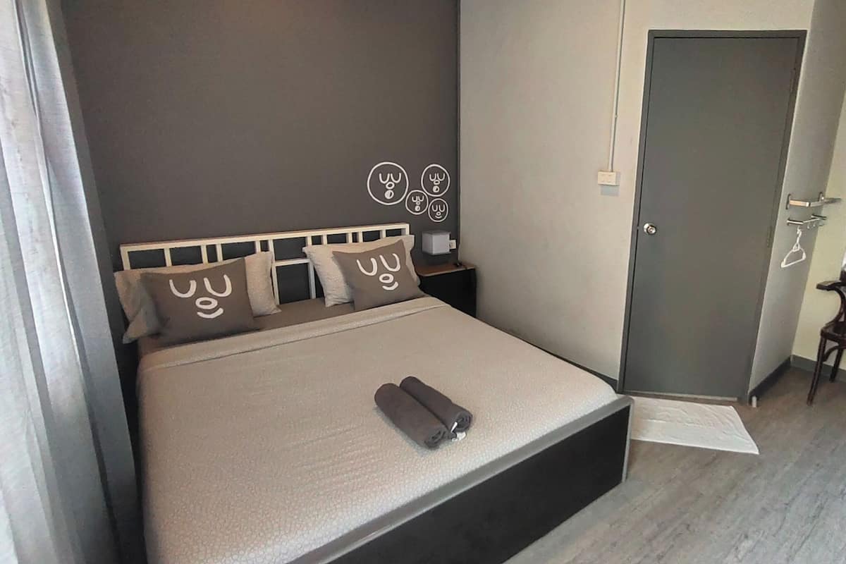 A bedroom with a bed, a bedside table, a chair, a door, and a small window.