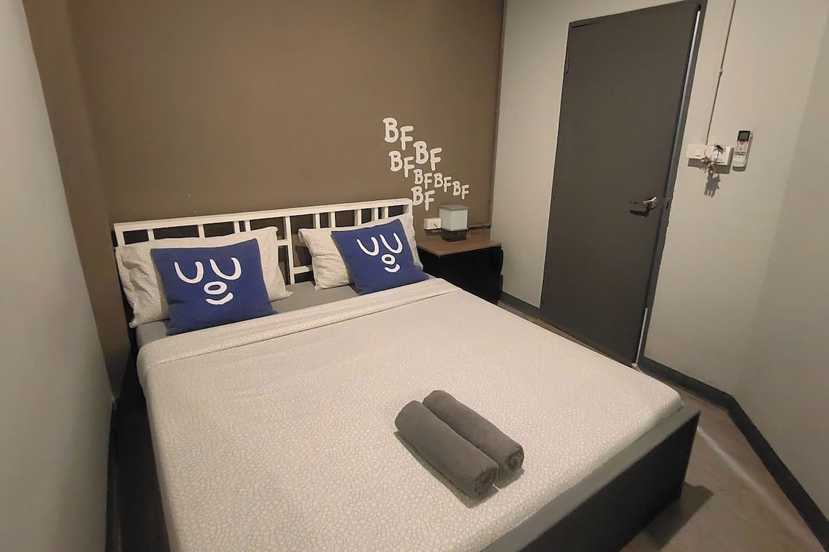 A neatly made bed with a white headboard, two blue pillows with white text, and a rolled-up towel.