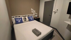 A neatly made bed with a white headboard, two blue pillows with white text, and a rolled-up towel. - Bed'S Friend (Bangkok)