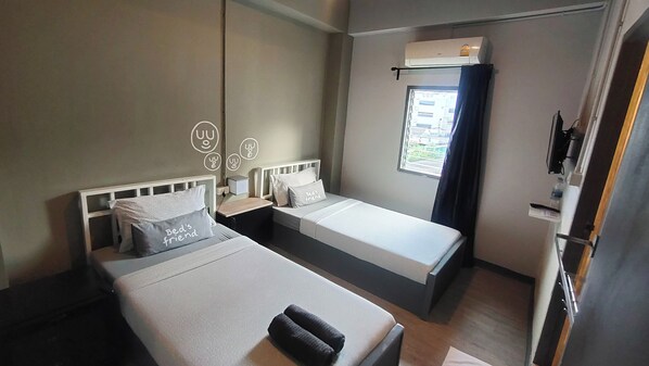 A hotel room with two single beds, a window with curtains, an air conditioning unit, and a bedside table with a lamp. - Bed's Friend (Bangkok)