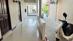 Un pasillo limpio y bien iluminado, con piso de baldosas, una patineta estacionada y una puerta a la izquierda.