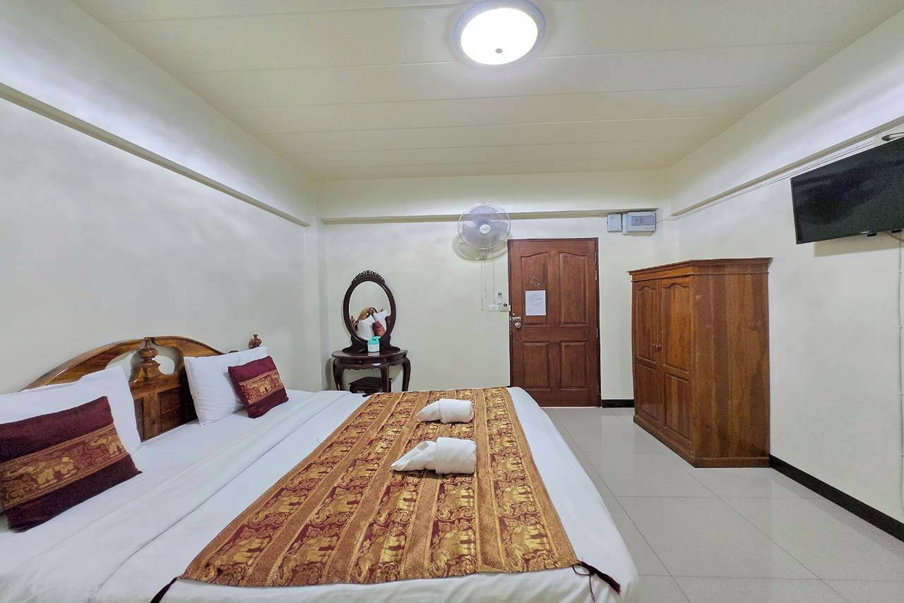 A hotel room with a bed, a wooden wardrobe, a television, and a ceiling fan.