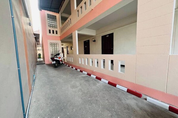 A corridor with a motorcycle parked on the left, leading to a building with multiple doors and windows. - Baan Sabai Guesthouse (Chiang Mai)
