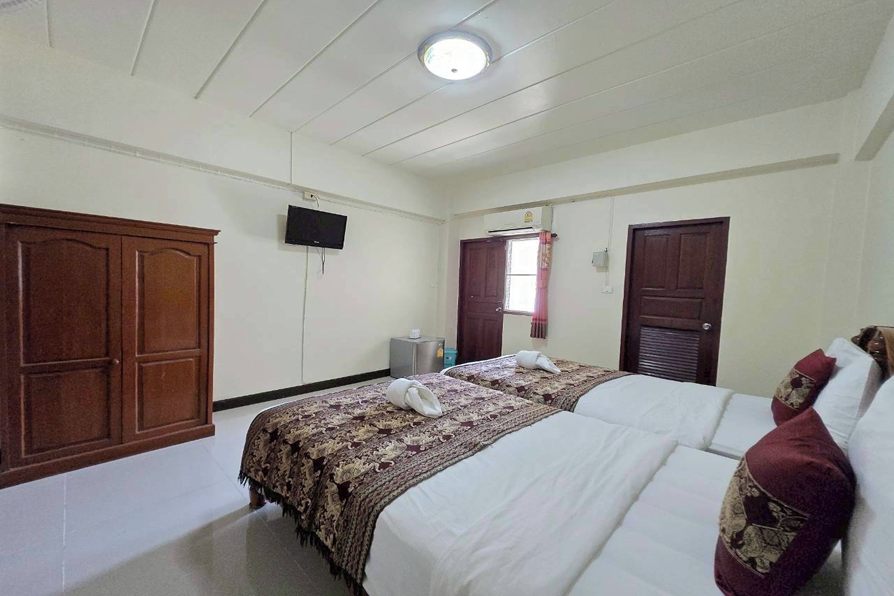 Una habitación de hotel con dos camas, un armario de madera, un televisor y una ventana con cortinas.