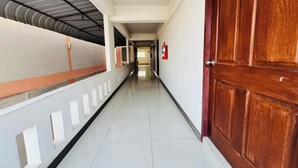 Un pasillo largo y estrecho con suelo de baldosas, paredes blancas y una puerta de madera a la derecha.