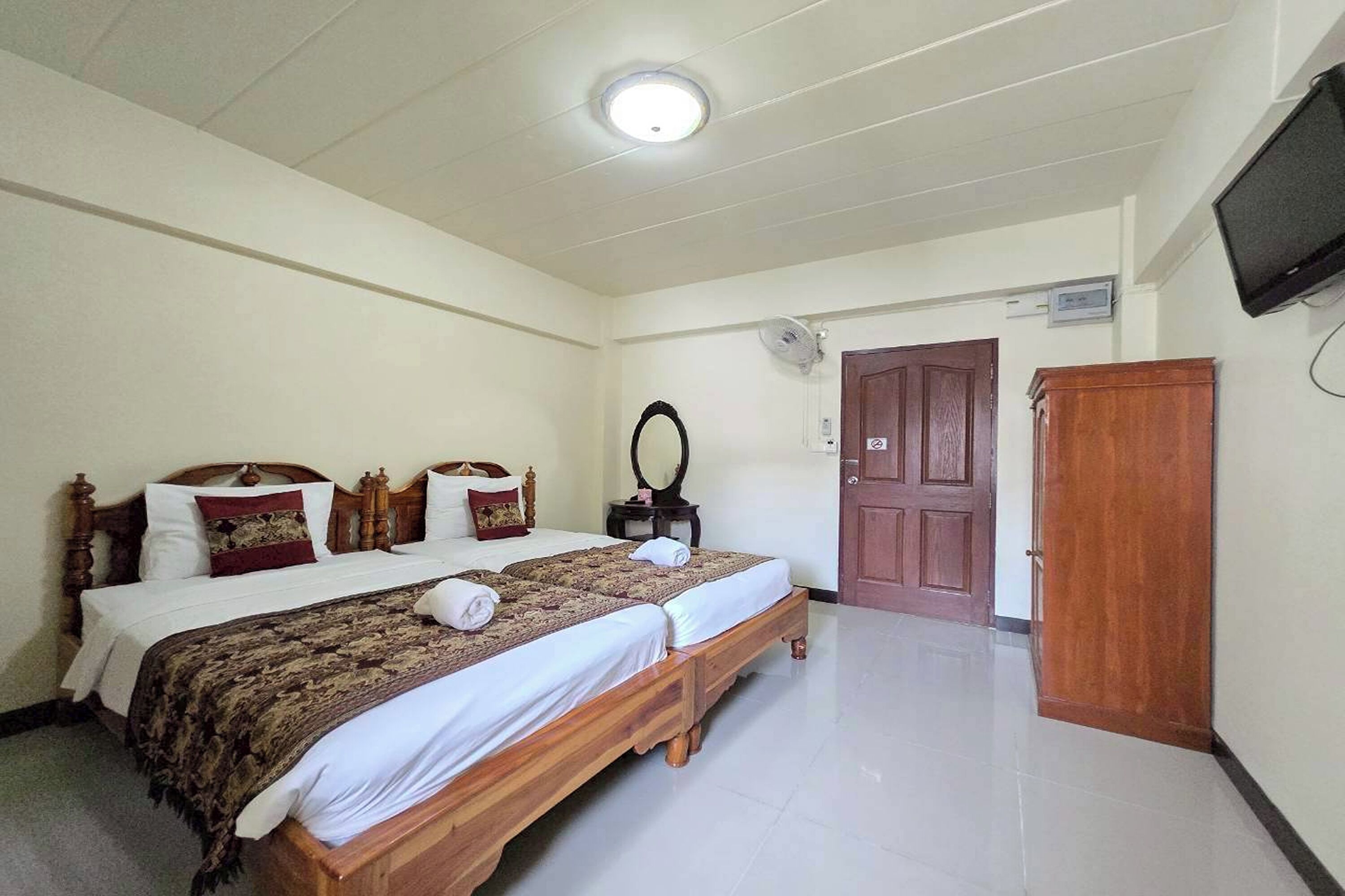 A bedroom with two wooden beds, a ceiling fan, a television mounted on the wall, and a wooden wardrobe.