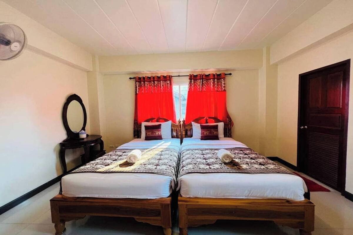 Una habitación con dos camas de madera, un espejo y un ventilador en la pared.