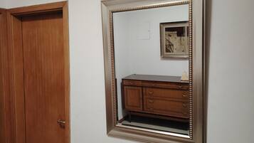 Una habitación con una puerta de madera, un espejo con un marco decorativo y un cuadro pequeño en la pared.
