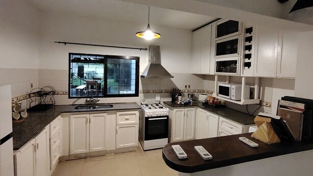 Una cocina con armarios blancos, estufa a gas, microondas y ventana con vistas a un jardín.
