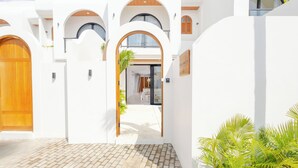A modern building with white walls, wooden doors, and arched windows. - Villa Amal 9 by Pertama Stay (Canggu)