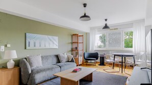 A modern living room with a grey sofa, wooden coffee table, and a bookshelf. There is a dining area with a table and chairs.