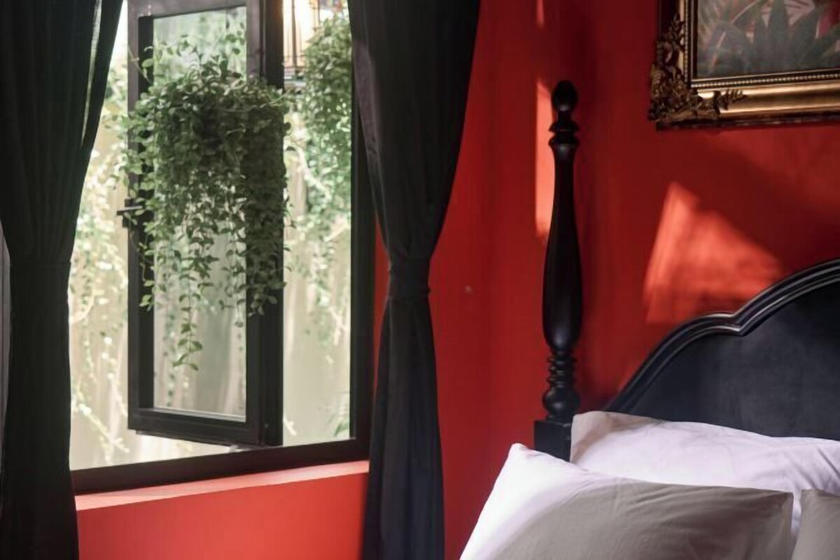 Una habitación con una cama, un ventanal con cortinas y una planta afuera.