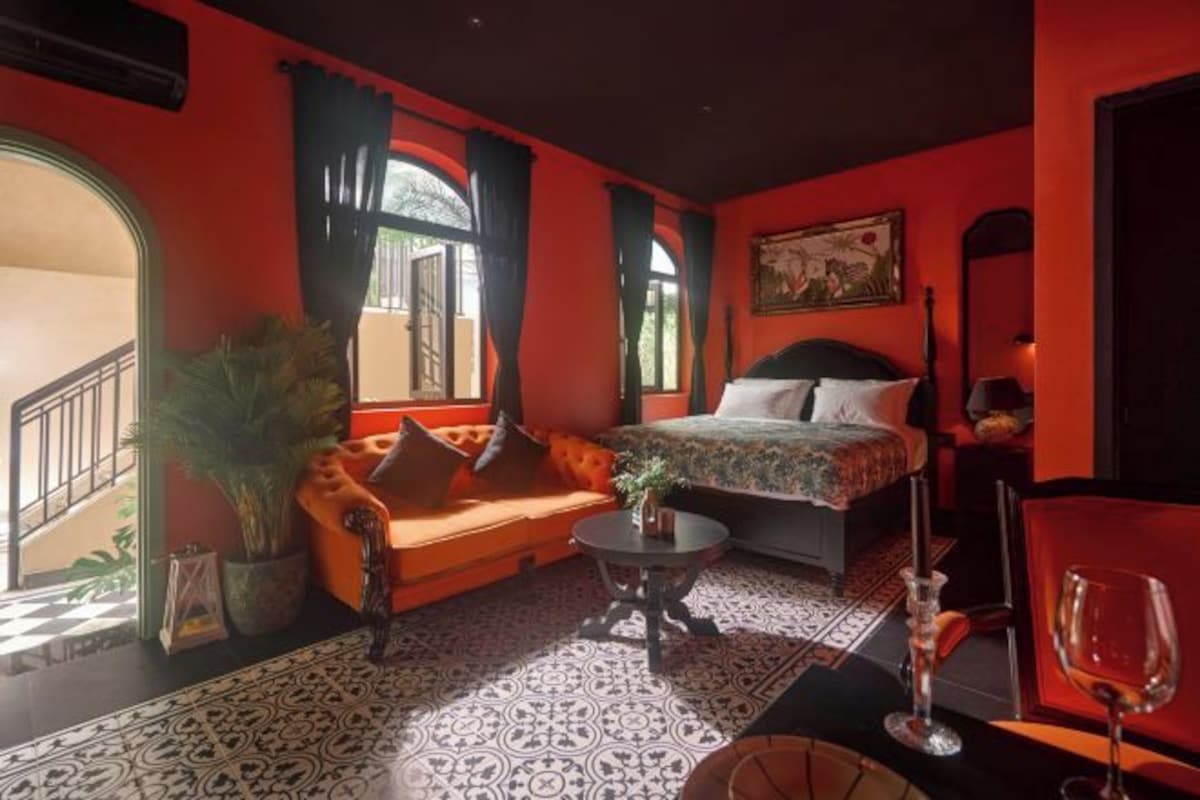 A room with a bed, a sofa, a small table, a potted plant, and a wine glass.