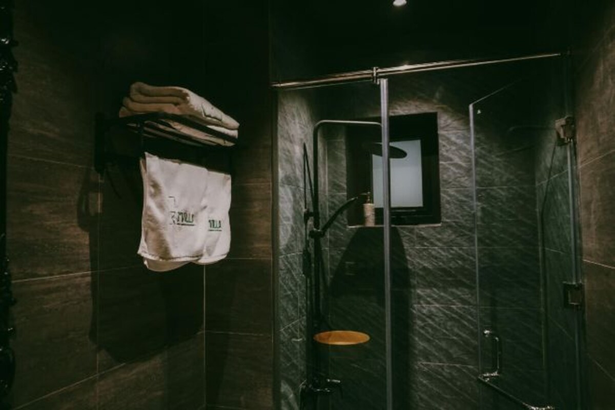 A modern bathroom with dark tiles, a glass shower enclosure, and a towel rack with a white towel.