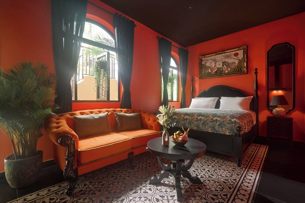 Een kamer met een bank, een bed, een tafel met een vaas en een kamerplant.