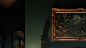 A bedroom with a bed, a nightstand with a lamp, a mirror, and a framed painting on the wall. - G'Villa Thao Dien (Ho Chi Minh City)