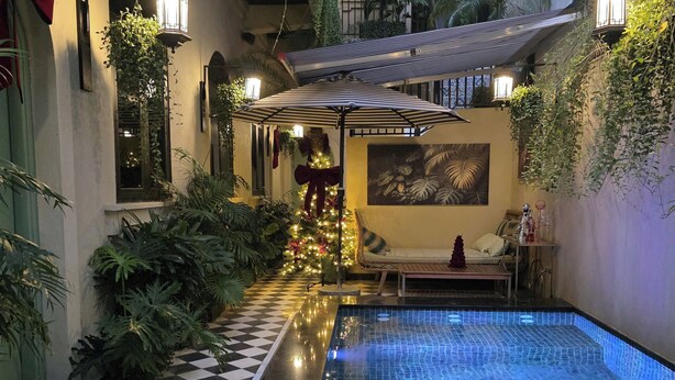 An indoor swimming pool with a checkered floor, surrounded by lush greenery and a cozy seating area with a Christmas tree. - G'Villa Thao Dien (Ho Chi Minh City)