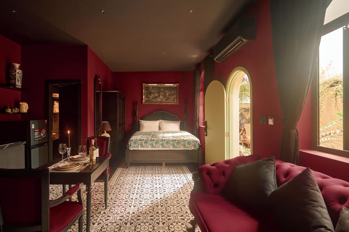 Een slaapkamer met een bed, een rode bank, een eettafel met stoelen en een vloer met een patroon.