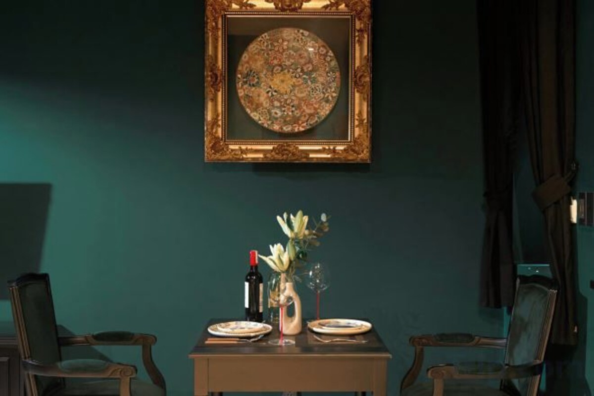 A dining area with a table set for two, a vase with flowers, and a framed artwork on the wall.