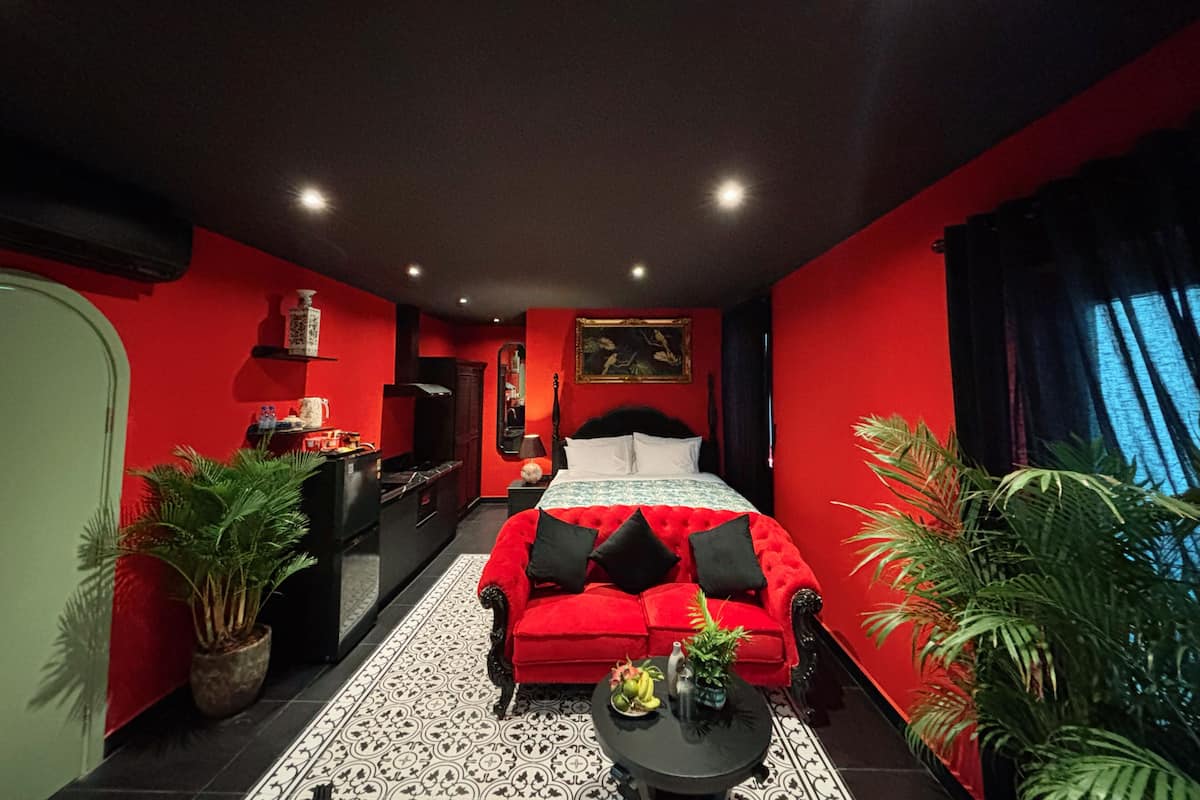 Een kamer met een rode bank, een bed, een kleine tafel met fruit en potplanten.