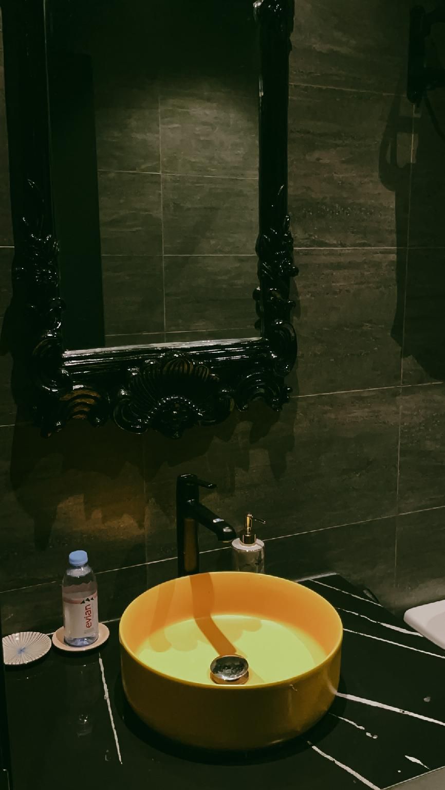 Een badkamer met een rond, geel wastafel, een zwart sierspiegel en een kraan.