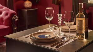 A dining table set with plates, glasses, cutlery, and a candle, in a room with red walls, a framed picture, and a window with curtains. - G'Villa Thao Dien (Ho Chi Minh City)