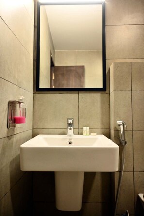 Une salle de bain avec un lavabo blanc, un miroir, une douchette à main et un distributeur de savon.