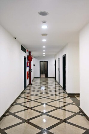 Un couloir avec un sol carrelé, un extincteur et une porte au fond.