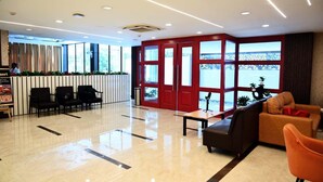 Un moderno vestíbulo de hotel con un mostrador de recepción, zona de estar y grandes ventanales que ofrecen vistas a un puente.