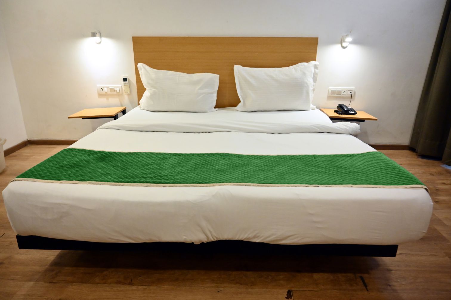 A large bed with white bedding and a green throw blanket, two bedside tables with lamps, and a wooden headboard.