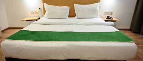 A large bed with white bedding and a green throw blanket, two bedside tables with lamps, and a wooden headboard.