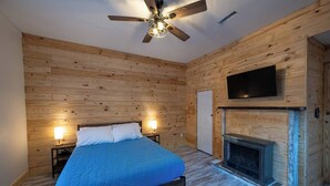 Ein Schlafzimmer mit Bett, Deckenventilator, Kamin und an der Wand montiertem Fernseher.