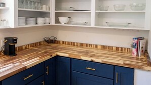 Eine Küche mit dunkelblauen Schränken, einer Holz Arbeitsplatte und weißen Regalen darüber.