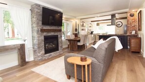 A modern living room with a stone fireplace, a flat-screen TV, a grey sofa, and a small wooden table.