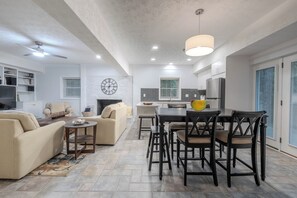A modern kitchen with a dining area, a living room with a sofa and a coffee table, and a large clock on the wall. - A Serene Retreat with Modern Comforts (Greer)