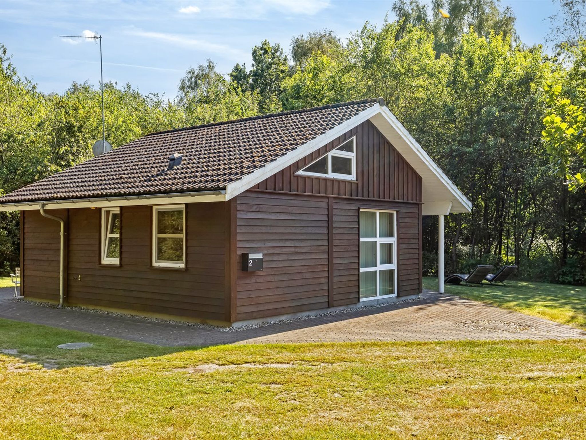 Ein eingeschossiges Holzhaus mit Ziegeldach, einer kleinen Veranda und der Hausnummer 2.